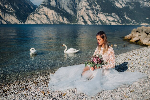 Une fille dans une robe blanche élégante est assise sur le quai du lac de Garde