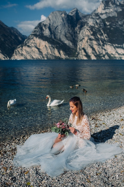 Photo une fille dans une robe blanche élégante est assise sur le quai du lac de garde