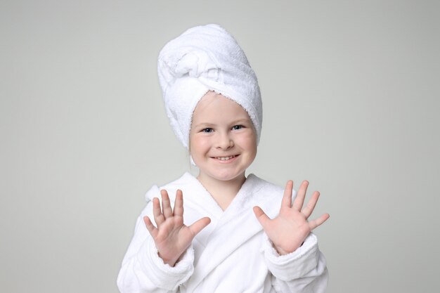 Fille Dans Une Robe Blanche Et Une Serviette Sur La Tête Après Une Douche Et Se Laver Les Cheveux. Cosmétique Enfant Et Soins De La Peau, Cures Thermales. Cheveux Propres Et Beaux.