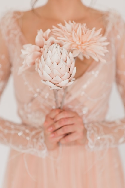 Une fille dans une robe chic tient des fleurs dans ses mains. Belles fleurs roses artificielles.