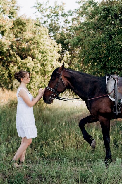 Fille dans une robe d'été blanche lors d'une promenade avec des chevaux bruns dans le village