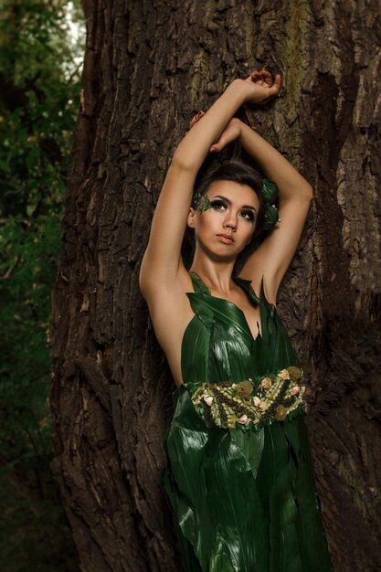 Fille dans une robe de feuilles de palmier vertes sur un lac forestier