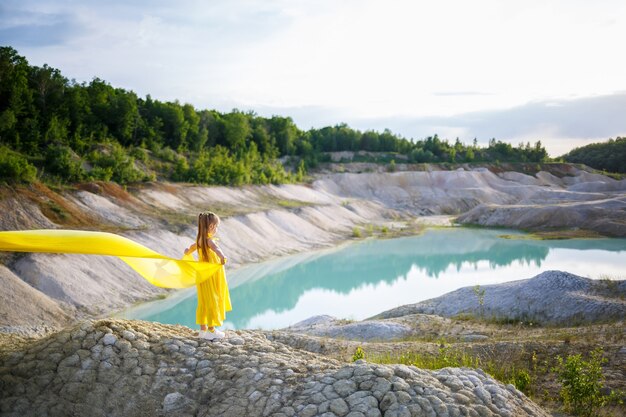 Fille dans une robe jaune avec des ailes dans un tissu jaune près du lac