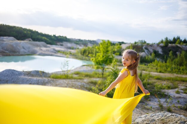 Fille dans une robe jaune avec des ailes dans un tissu jaune près du lac