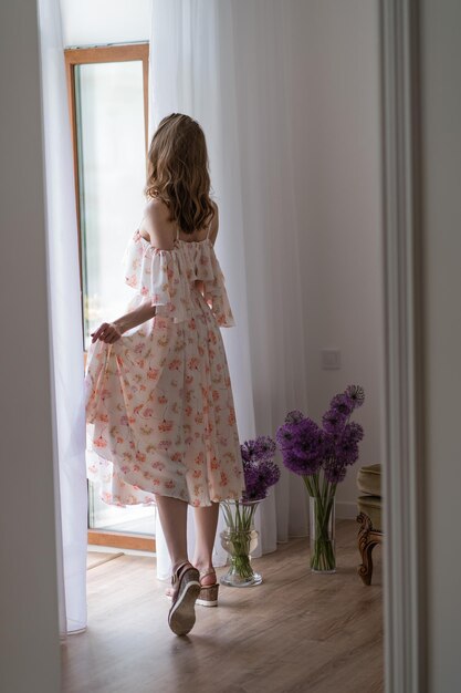 La fille dans une robe légère se tient sur le balcon avec son dos