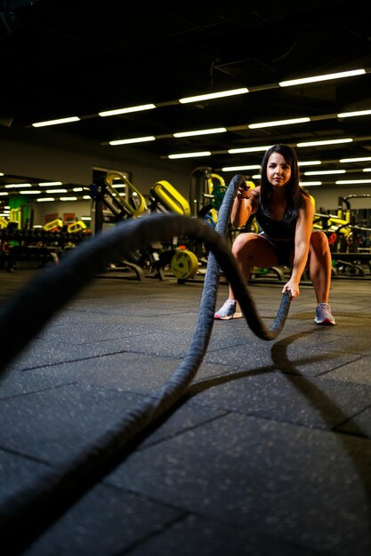 La fille dans la salle de gym fait un exercice avec des cordes dans les mains