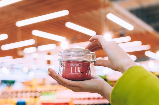 Une fille dans un supermarché tient un bocal en verre avec du miel en gros plan. sur fond de lampes.