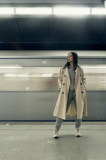 Fille dans un trench-coat beige dans le métro attendant le train sur le quai