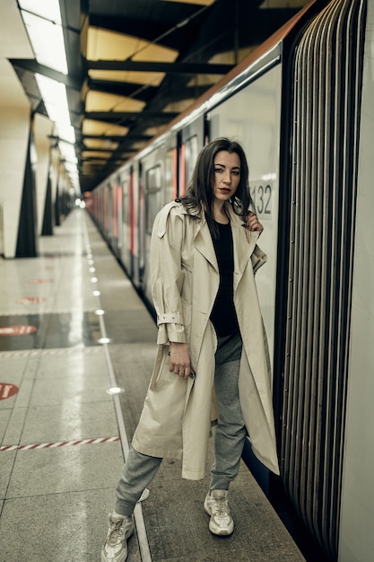 Fille dans un trench-coat beige dans le métro attendant le train sur le quai