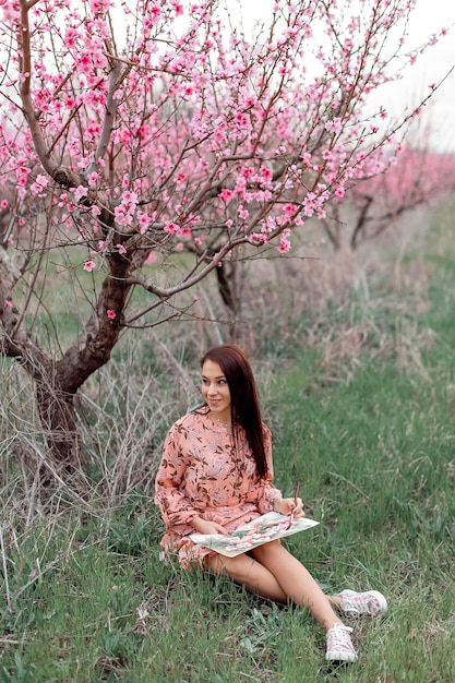 Une fille dans un verger de pêchers en fleurs se repose sous un arbre assis et dessinant