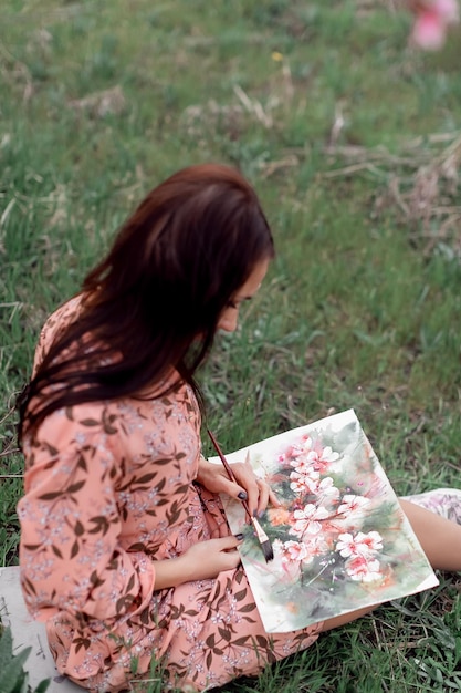 Une fille dans un verger de pêchers en fleurs se repose sous un arbre assis et dessinant