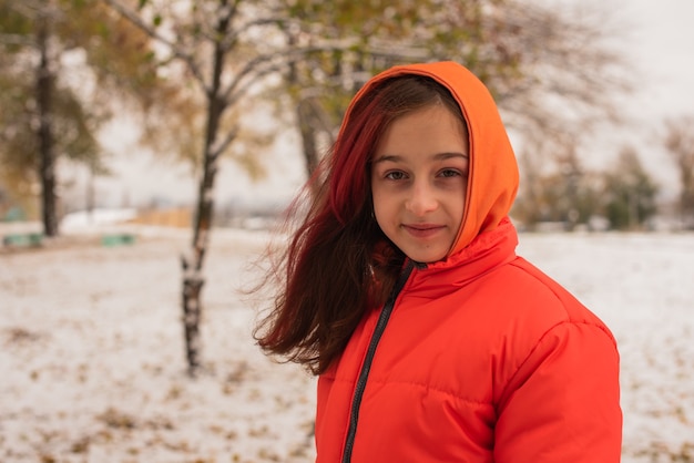 Une fille dans une veste chaude orange vif. Fille dans une veste orange par temps de neige. Adolescente en hiver