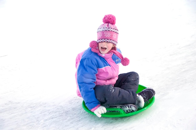 Une fille dans une veste d'hiver qui crie descend d'une glissade de neige