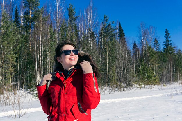 La fille dans une veste rouge marche dans les bois et apprécie le soleil de ressort