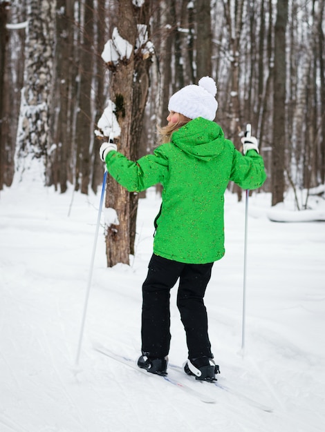 Fille dans une veste verte ski dans la forêt d'hiver