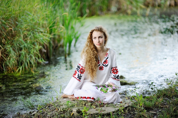 Fille dans les vêtements nationaux ukrainiens avec des couronnes de fleurs sur la rive