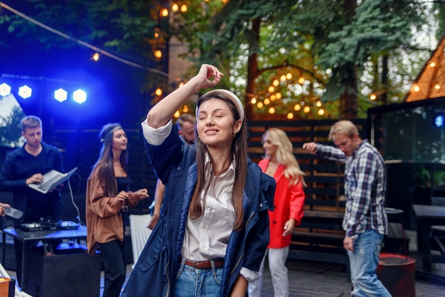 Fille dansant au premier plan pendant que ses amis dansent à la lumière des lampes colorées pendant la fête de célébration à l'extérieur.