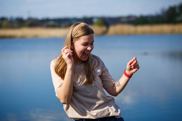 Fille dansant près du lac, temps ensoleillé. Une jeune femme se réjouit de la vie, danse et chante. Elle est de bonne humeur et le sourire aux lèvres.