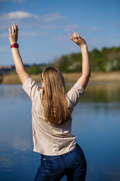 Fille dansant près du lac, temps ensoleillé. Une jeune femme se réjouit de la vie, danse et chante. Elle est de bonne humeur et le sourire aux lèvres.