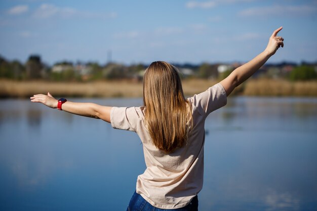 Fille dansant près du lac, temps ensoleillé. Une jeune femme se réjouit de la vie, danse et chante. Elle est de bonne humeur et le sourire aux lèvres.