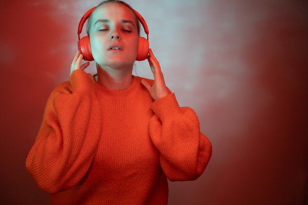 La fille danse dans un éclairage de couleur vive et écoute de la musique avec des écouteurs