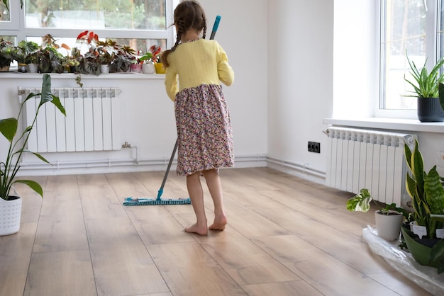 Une fille danse avec une vadrouille pour nettoyer le sol dans une nouvelle maison nettoyage général dans une pièce vide la joie de déménager aide aux tâches ménagères