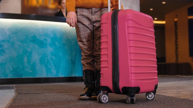 Une fille debout avec un bagage rose à l'hôtel