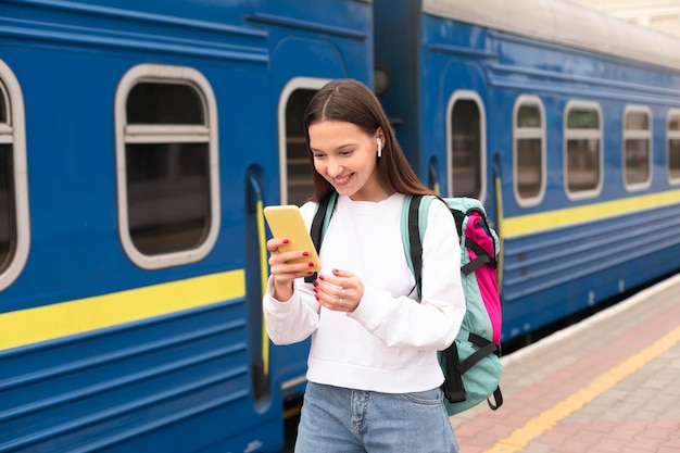 Photo fille debout à côté du train et à l'aide de téléphone mobile