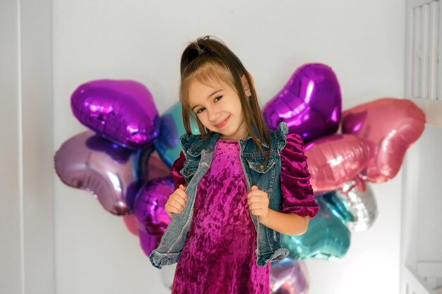 Fille debout devant un mur décoré avec des ballons en aluminium en forme de coeur