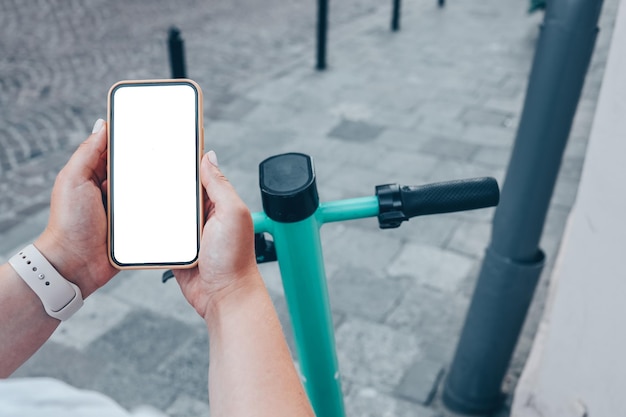 Fille debout avec un scooter électrique et montrant le téléphone avec un écran blanc vierge