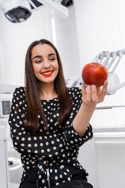 Fille debout en stomatologie avec pomme dans les mains Outils dentaires modernes sur fond flou Concept de dents saines