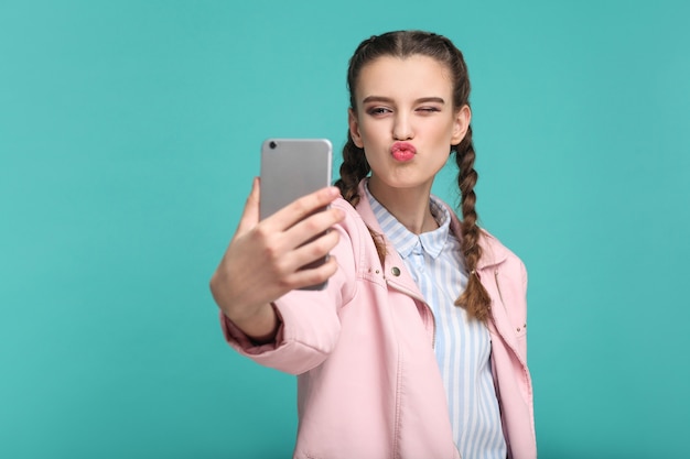 Fille debout tenant un téléphone intelligent mobile et faisant un selfie ou un appel vidéo avec un baiser