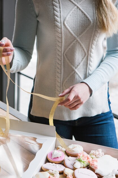 Fille décorant la boîte en pain d'épice avec ruban. Courrier féminin, gros plan de cuisson, dessert sucré, concept de nourriture savoureuse