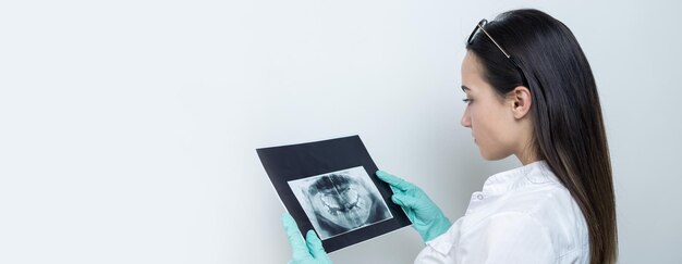 Une fille dentiste en blouse blanche tient un instantané des dents du patient.