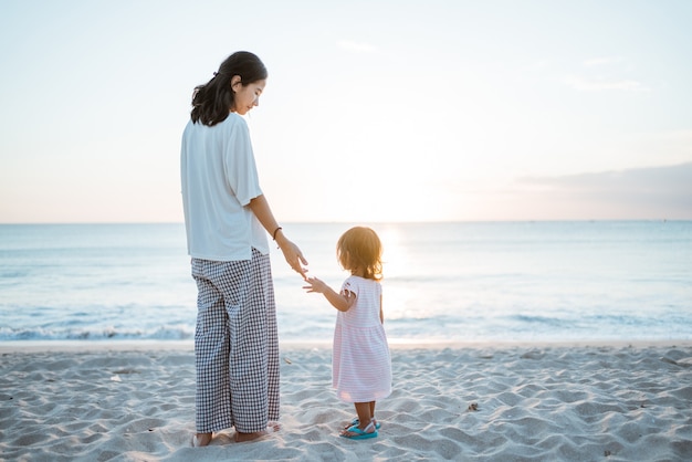 Fille de derrière et une robe blanche debout sur une plage d'été en regardant le coucher du soleil