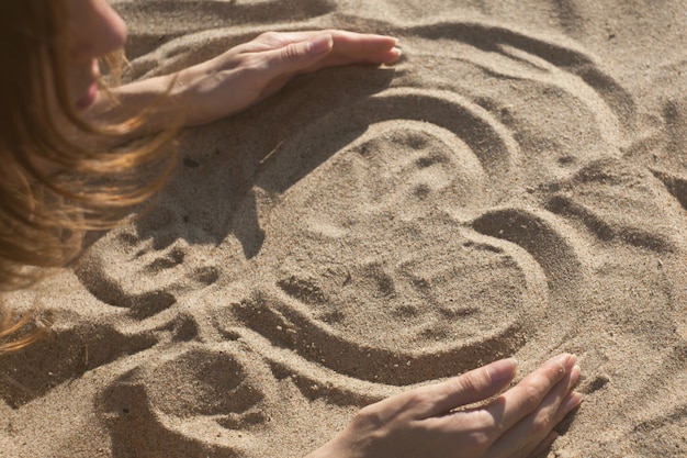 Photo fille dessinant un coeur sur le sable au coucher du soleil dans un concept d'amour d'été