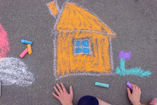 Une fille dessine un arc-en-ciel une maison avec de la craie sur le trottoir