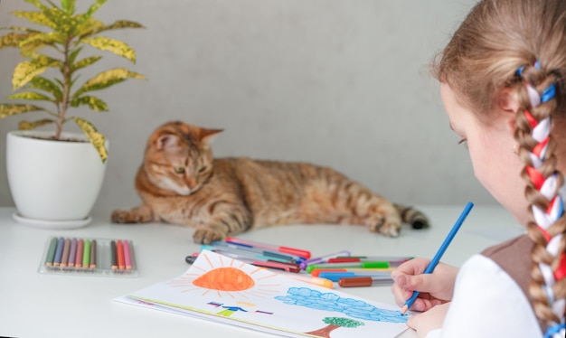 Une fille dessine un dessin et un chat est allongé sur la table