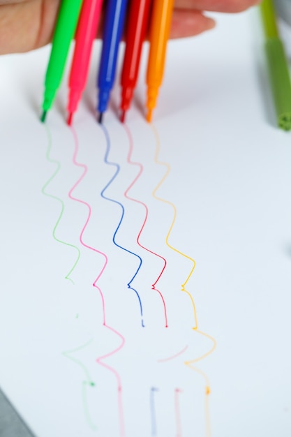 La fille dessine avec des feutres multicolores sur du papier blanc