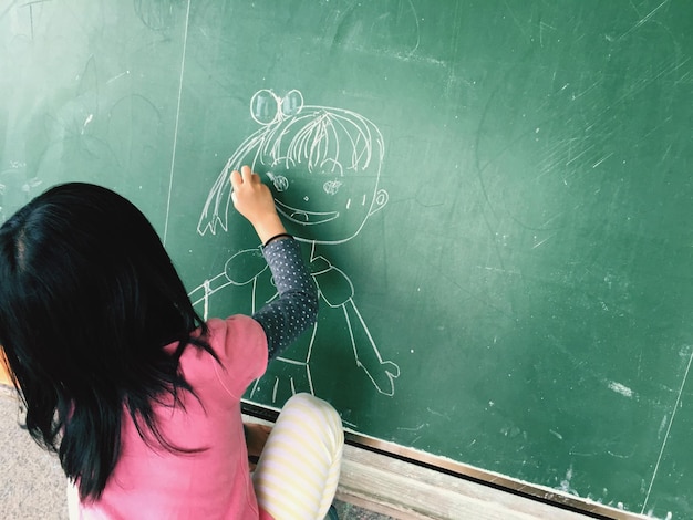 Une fille dessine sur le tableau en classe.