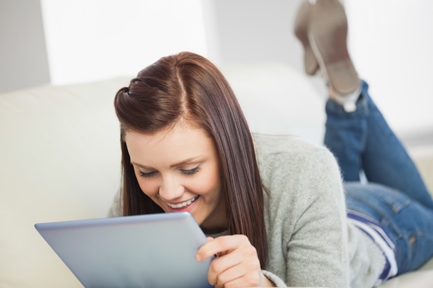 Fille détendue regardant et en utilisant un tablet pc sur un canapé