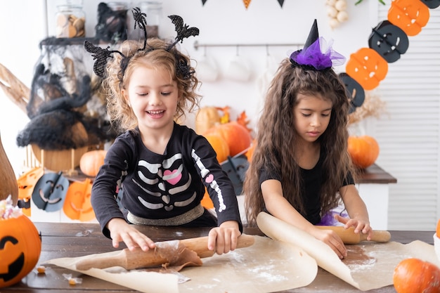 Fille de deux enfants en costume de sorcière, préparant des biscuits, s'amusant dans la cuisine, célébrant Halloween.