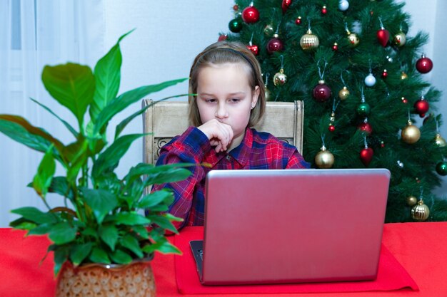 La fille discute sur l'ordinateur portable à l'arrière-plan de l'arbre de Noël