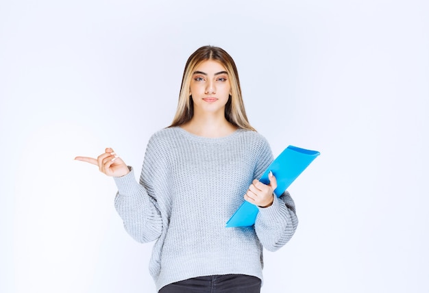 Fille avec un dossier bleu pointant vers quelqu'un de côté.