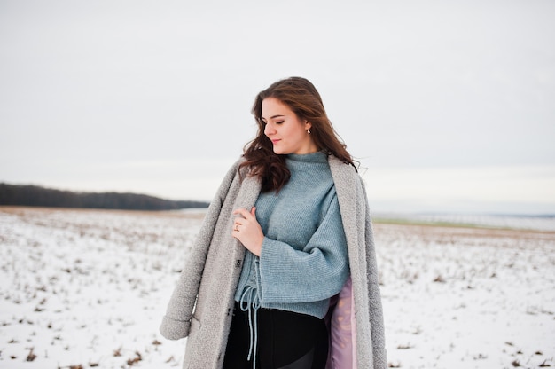 Fille douce en manteau gris contre le paysage de neige.