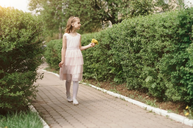 Fille douce souriante avec un bouquet de pissenlits marchant le long de th