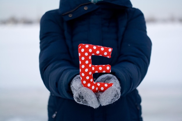 Fille en doudoune bleue et gants tenant une lettre de tissu E