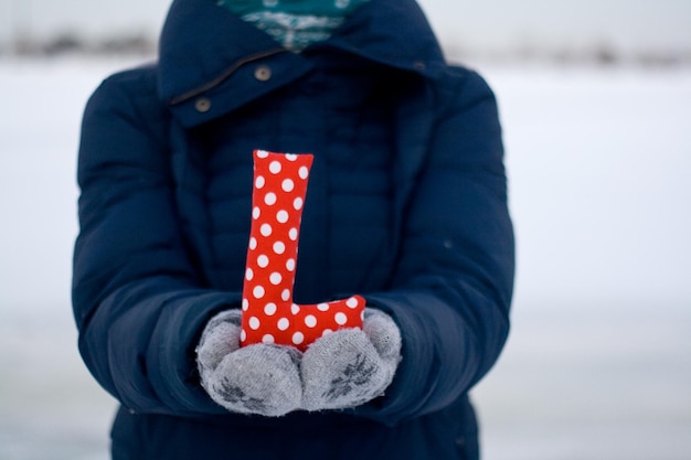 Fille en doudoune bleue et gants tenant une lettre de tissu L