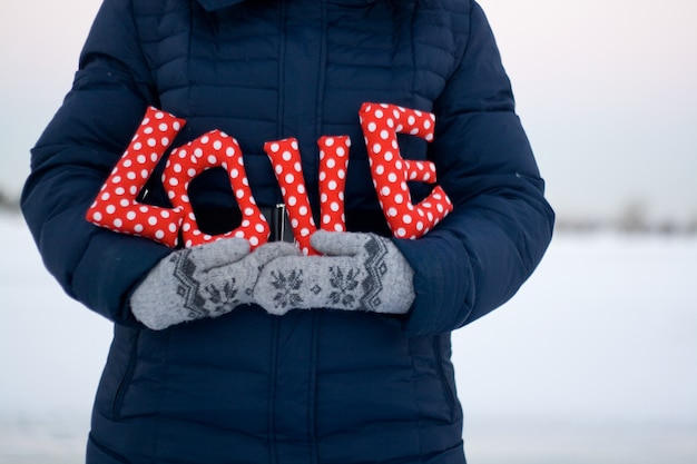 Fille en doudoune bleue et gants tenant une pancarte "Love"