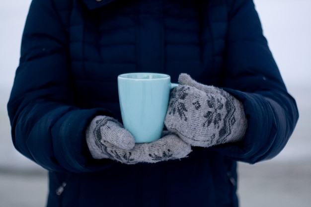 Fille en doudoune bleue et gants tenant une tasse de thé bleue